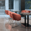 Air seating niko lounge chair soft seating in orange peach fabric with a black skid base in an interior cafe setting, with marble grey flooring, modern interior