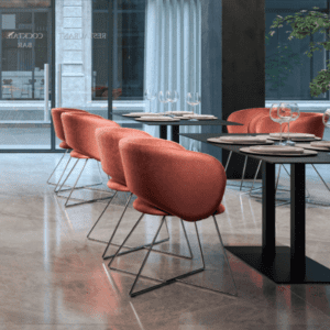 Air seating niko lounge chair soft seating in orange peach fabric with a black skid base in an interior cafe setting, with marble grey flooring, modern interior