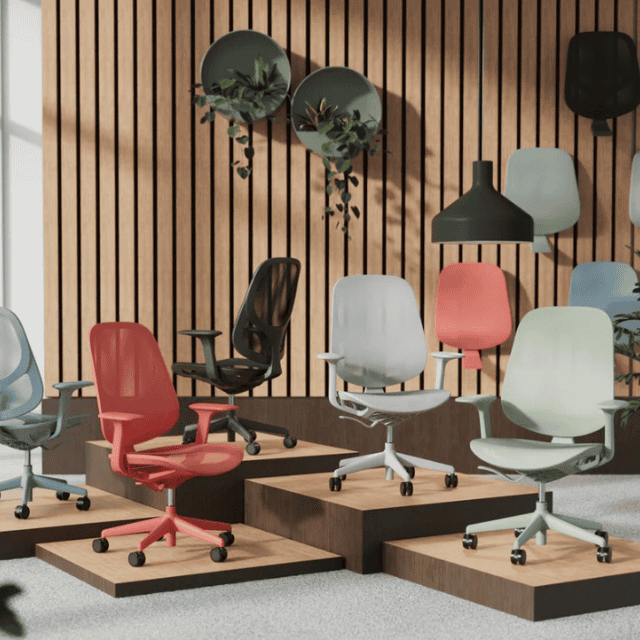 Dynamic seating Tutti mesh chairs in coral, black, mint, grey and blue on podiums showing different angles of the chair with a panelled back drop with a lamp, decorative plants and the seat backs.