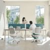 edit office ux mesh chair in white side with a person sitting talking to another person across the desk in an office environment with blue desk mounted screens