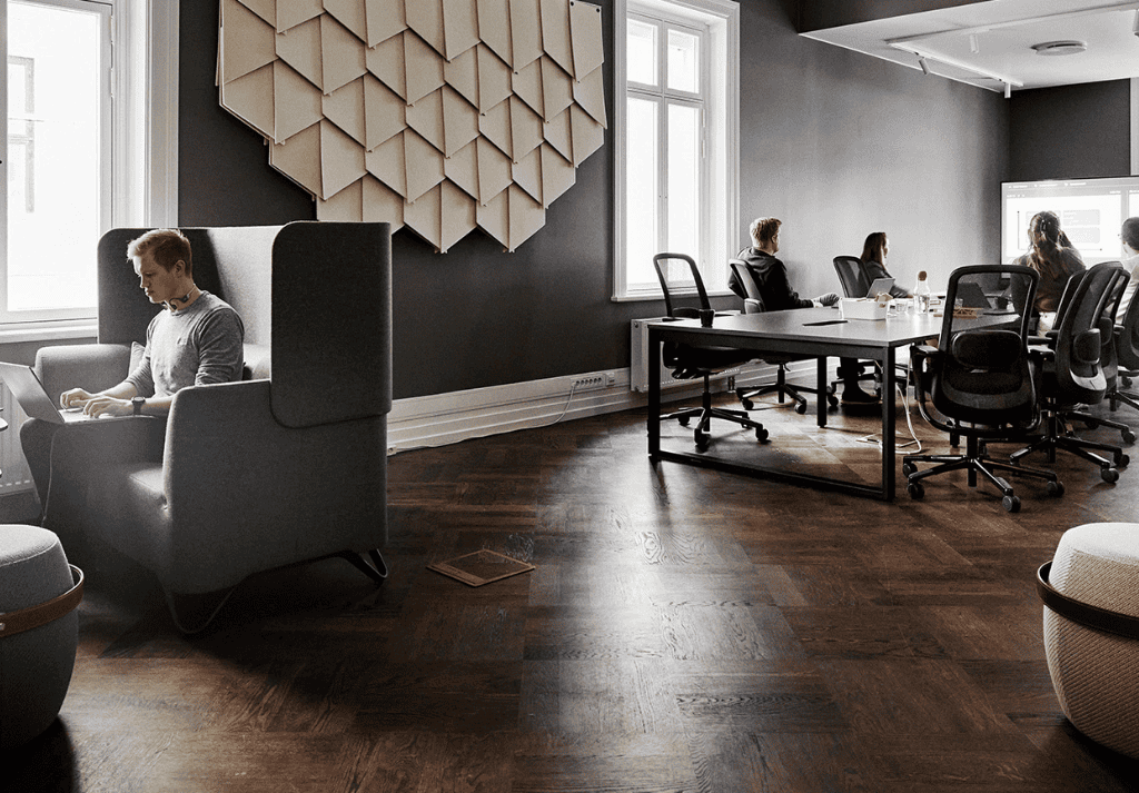 Open-plan office with banquette seating and high-back soft seating creating a casual collaboration zone while maintaining visual openness