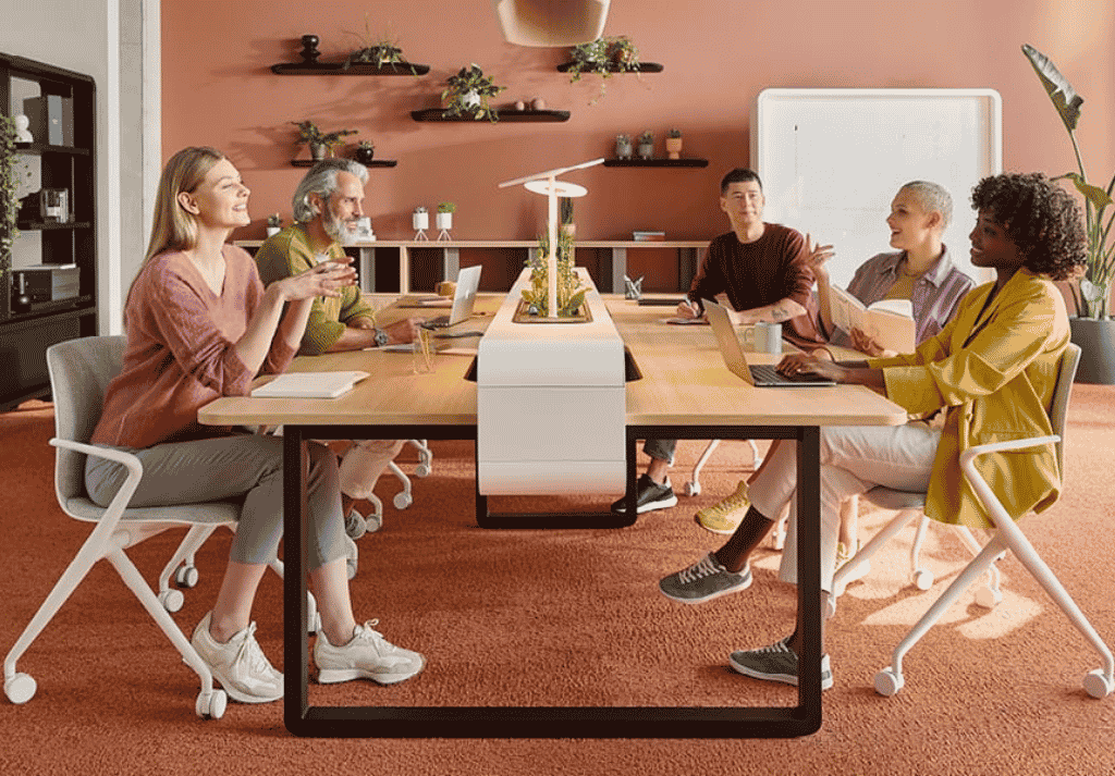 Office team collaborating at shared bench desks in an open plan workspace, discussing ideas and working together in a modern environment