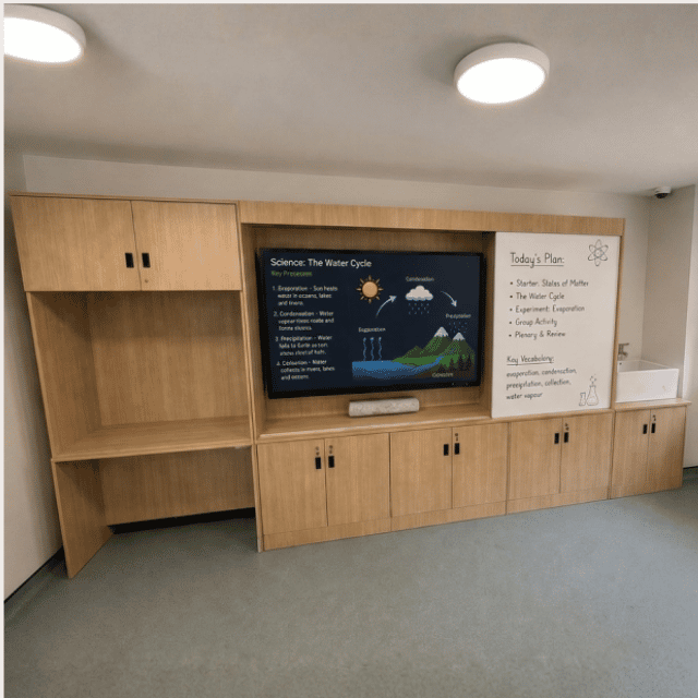 A comprehensive, floor-to-ceiling modular teacher storage wall installed at Octavia School by BT Office Furniture. The custom multi-functional unit features built-in dry-erase whiteboards, integrated open book shelving, and secure lower cupboards under a clean laminate finish.